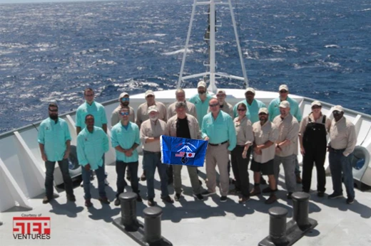The 2017 discovery team on the bow of the ship, holding a flag