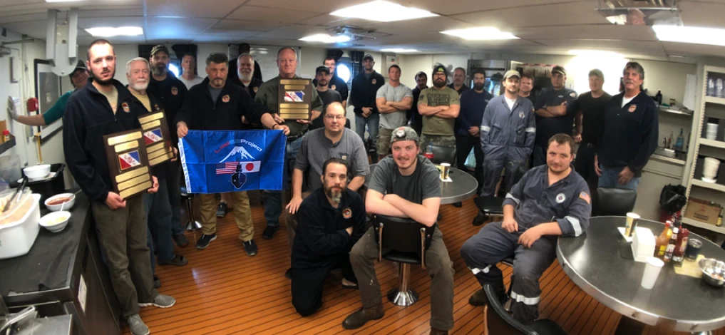 The 2019 discovery team in the ship's mess, holding the Lost 52 Project flag and three plaques